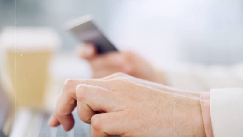 A Close-Up of Someone Typing on A Laptop While Holding a Smartphone, Likely Managing Online Transactions or Payments