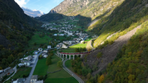 A Train Passes Through a Swiss Village Surrounded by Mountains, Capturing a View You Can See During One Week in Switzerland