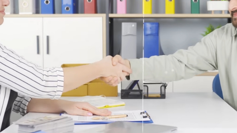 Two People Shaking Hands at A Desk, Likely Finalizing an Agreement, with Paperwork and Office Supplies in The Background