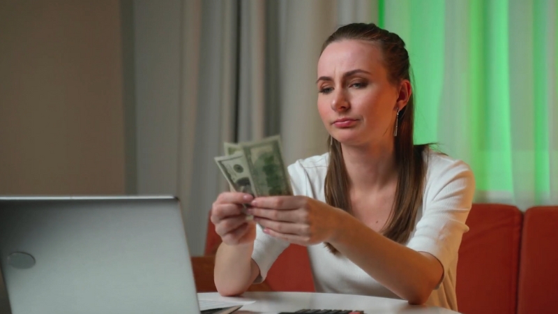 A Woman Sitting at A Table, Counting Dollar Bills