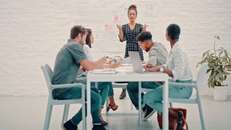 A team meets in a modern office as one person presents campaign ideas on a whiteboard during a creative strategy session