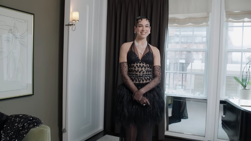 Dua Lipa wearing a black feathered Chanel dress with sheer gloves and layered diamonds at the Met Gala 2025