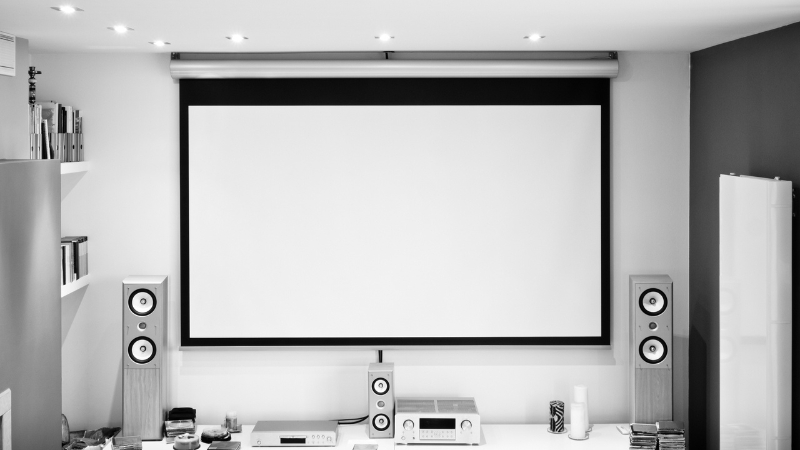 A minimalist room with a retractable projector screen and built-in speakers