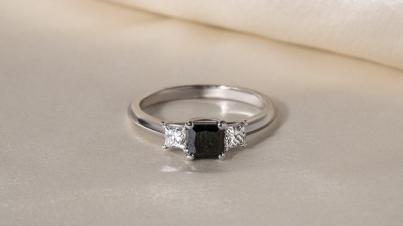 A lab-grown black diamond ring with two clear side stones set in a sleek white metal band