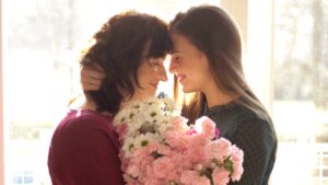 A mother and daughter sharing a joyful moment, with the daughter holding a bouquet of flowers for Mother’s Day