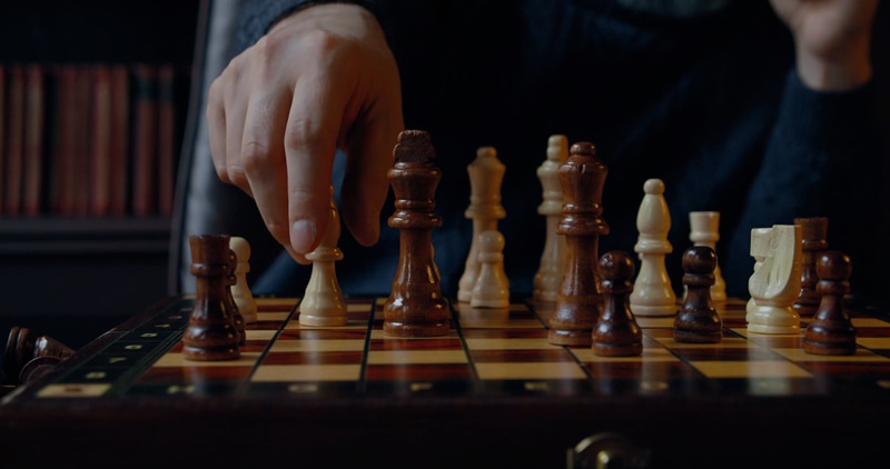 Close-up of a person making a move on a wooden chessboard, highlighting chess as one of their intellectual hobbies