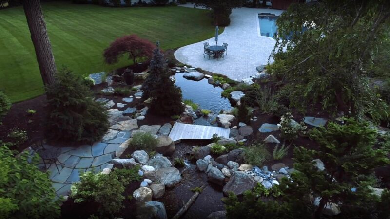 Backyard with koi pond, small footbridge, stone landscaping, and poolside dining area
