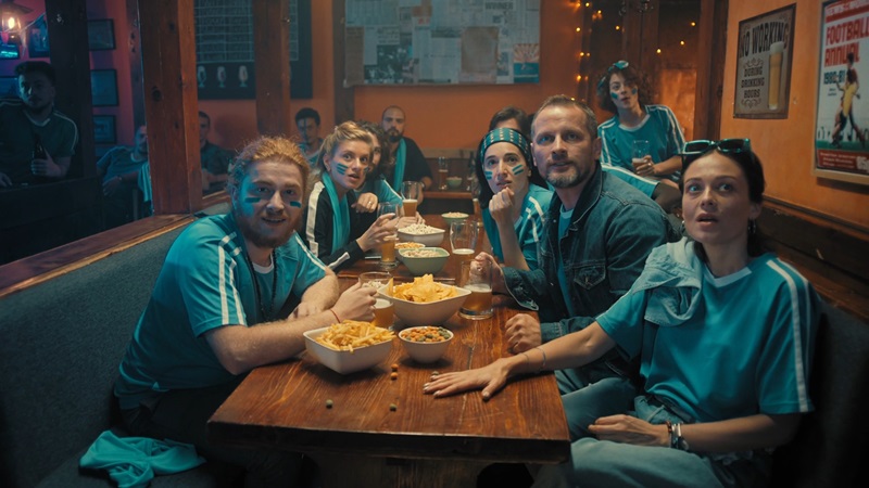 Group of friends in matching jerseys gathered at a pub, watching a sports game and enjoying snacks, sharing one of their favorite social hobbies