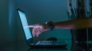 Person touching laptop screen in dark room showing interactive marketing in action