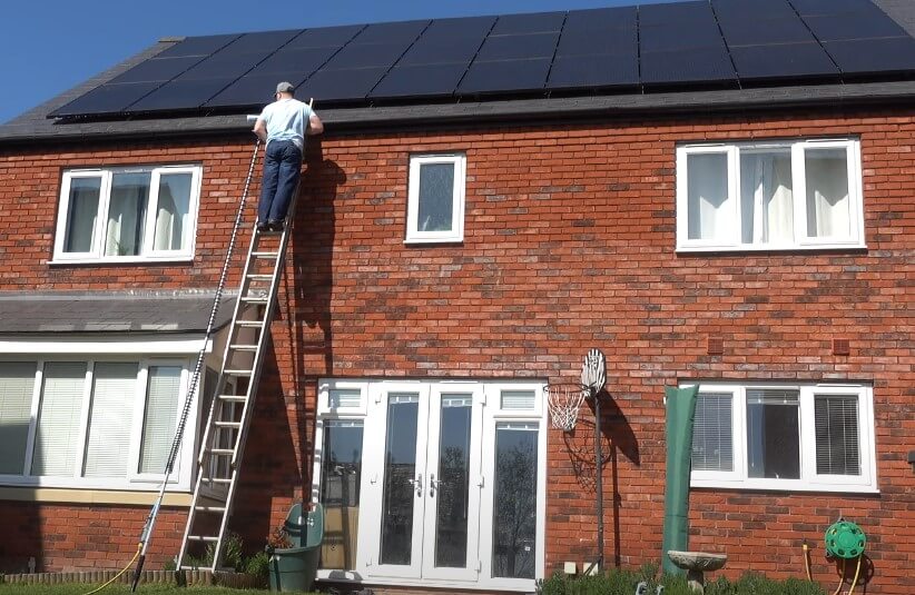 A worker climbs a ladder to maintain solar panels on a residential roof