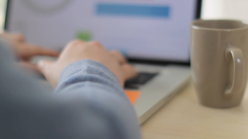 A person works on a laptop next to a coffee mug while setting up an online course