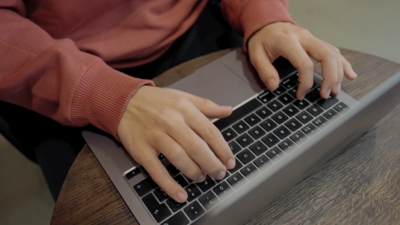 A person in a red sweater types on a laptop at a small round table