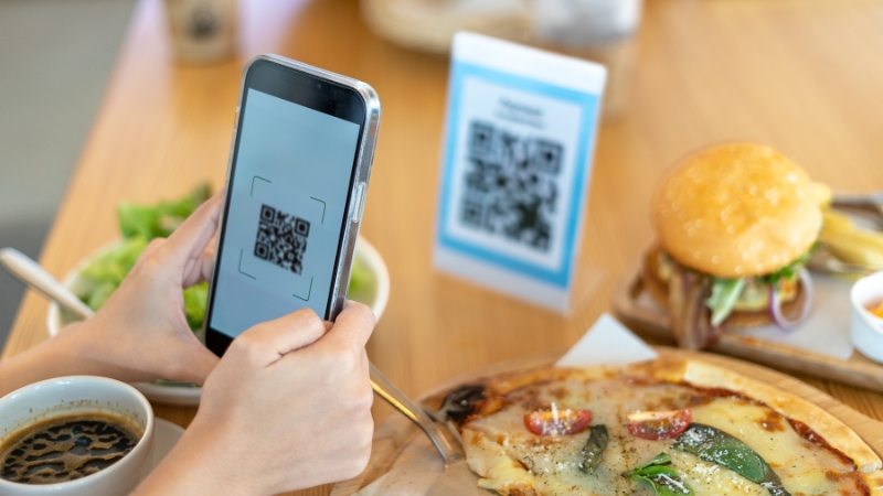 Person scanning a QR code at a restaurant table as part of hybrid interactive marketing