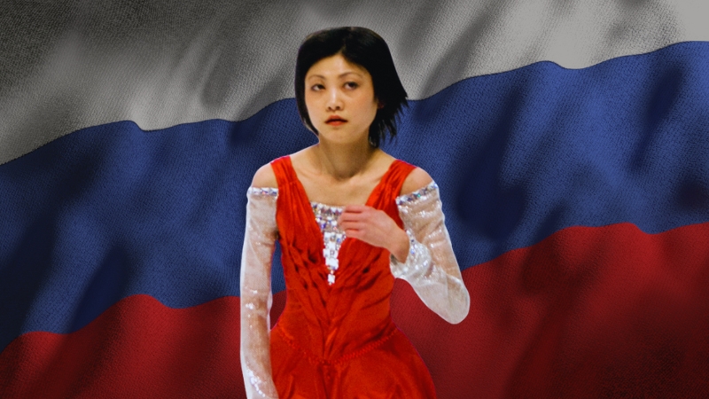 Yuko Kawaguti stands in a red skating costume in front of the Russian flag