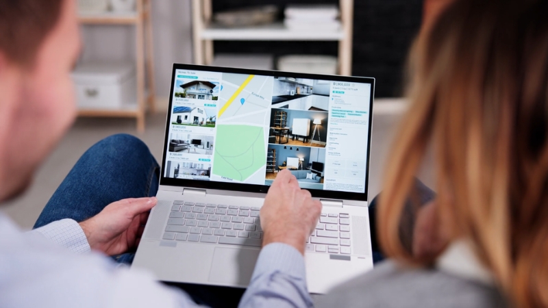 Two people review property listings on a laptop, planning to act fast on properties below market price