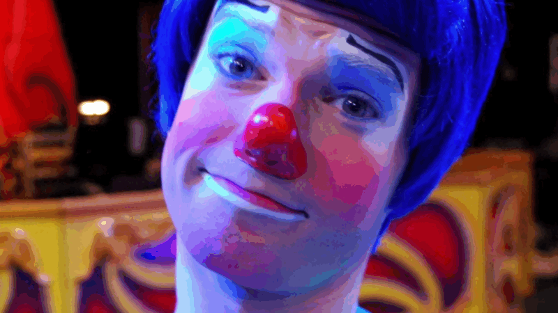 A close-up of a clown with blue hair and a red nose