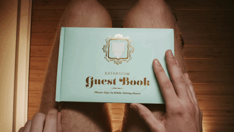 A person holding a mint green bathroom guest book while sitting on a toilet