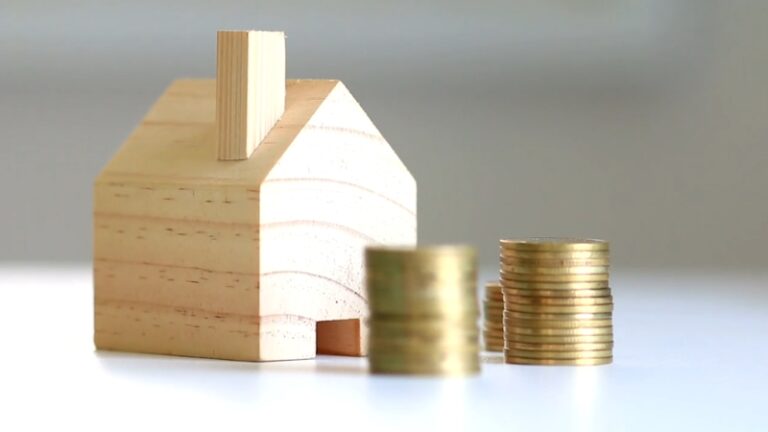 A small wooden house and stacks of coins illustrate the concept of properties below market price for real estate investors