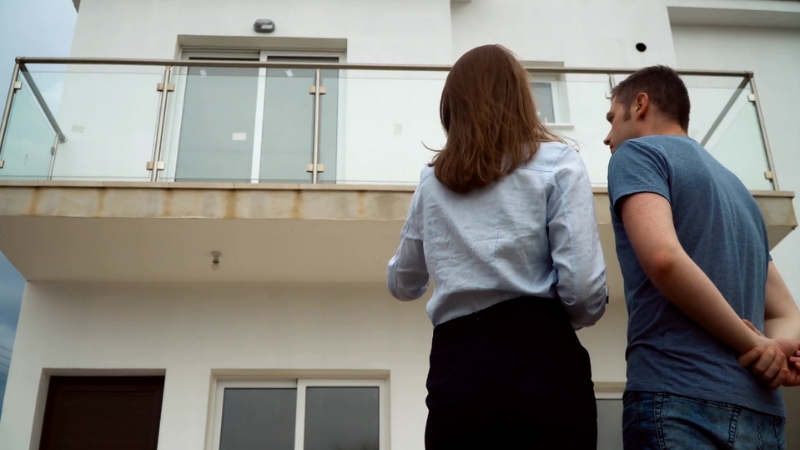 Two people stand outside a modern house, discussing investor strategies for properties below market price