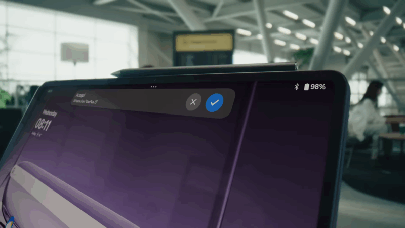The OnePlus Pad 3 shows a file transfer notification on its display while connected to another device in a bright airport lounge