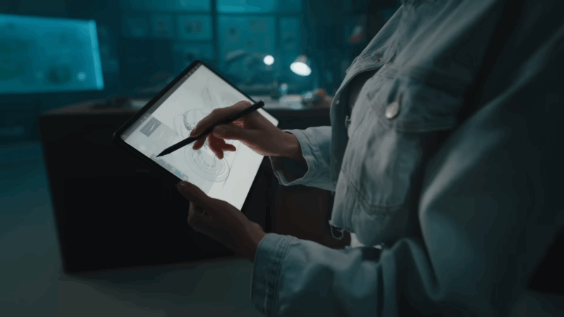 A person uses a stylus to sketch detailed designs on the bright display of the OnePlus Pad 3 in a dimly lit workspace