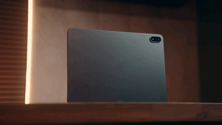 The OnePlus Pad 3 sits on a wooden shelf showing its slim all-metal back with the rear camera and OnePlus logo clearly visible