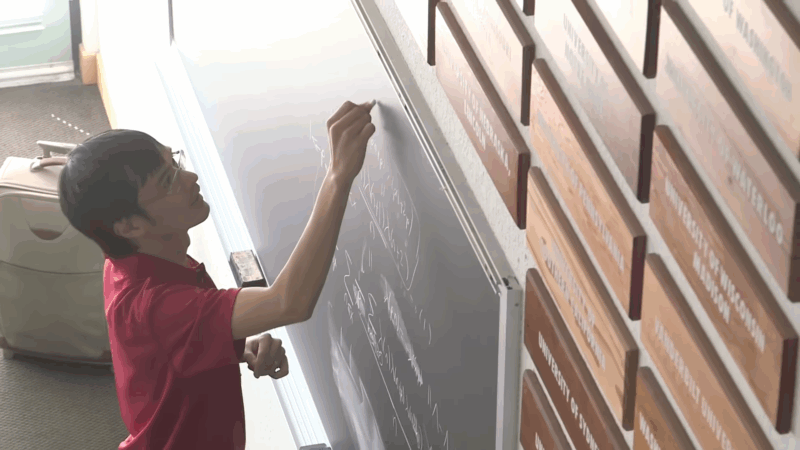 Terence Tao writes on a chalkboard filled with equations during a lecture at an academic event