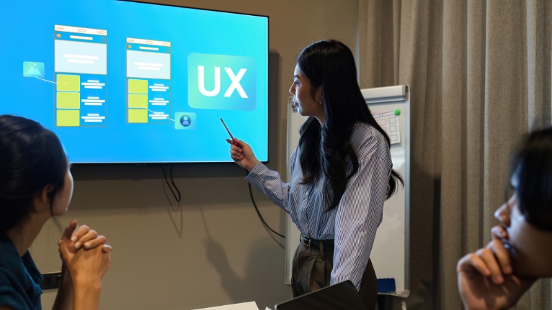 A woman presents a UX flow on a large screen to a team