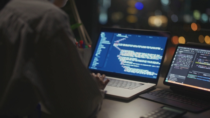 A person works on two laptops with code displayed, symbolizing a field guide to leading with AI in the workplace