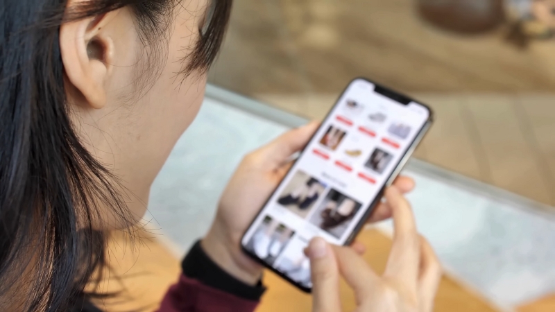A woman browsing an online store on her smartphone, scrolling through product listings