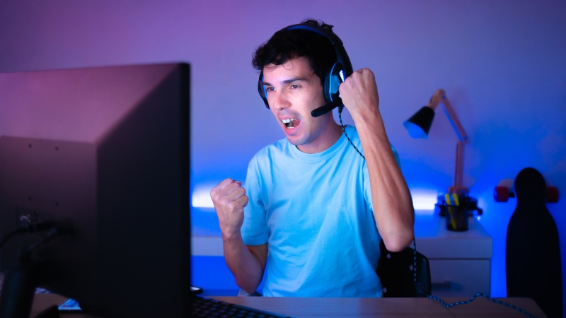Excited gamer with headset celebrating a win while playing on a desktop computer