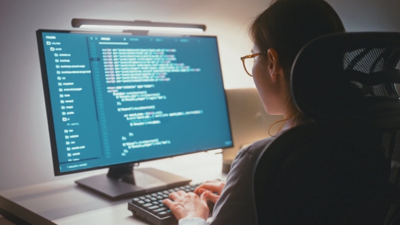 A woman works at a computer with code on the screen, representing the next five years of AI in the workplace