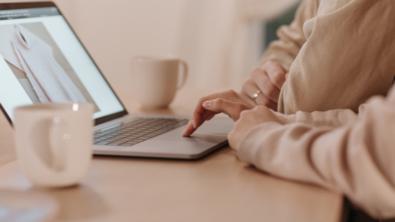 Two people browsing an online clothing store on a laptop with coffee mugs on the table