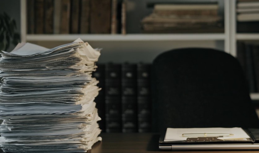 A stack of papers rests on a desk in front of an open laptop