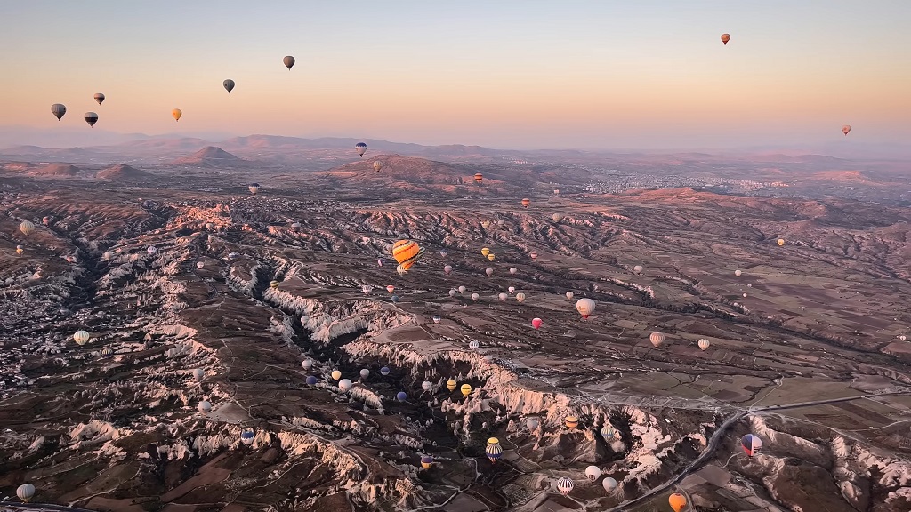 Sunrise view of Cappadocia, Turkey with dozens of colorful hot air balloons floating above unique rock formations and valleys