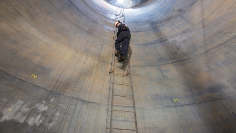 Worker climbs a tall ladder inside a confined space as part of emergency preparedness and rescue planning