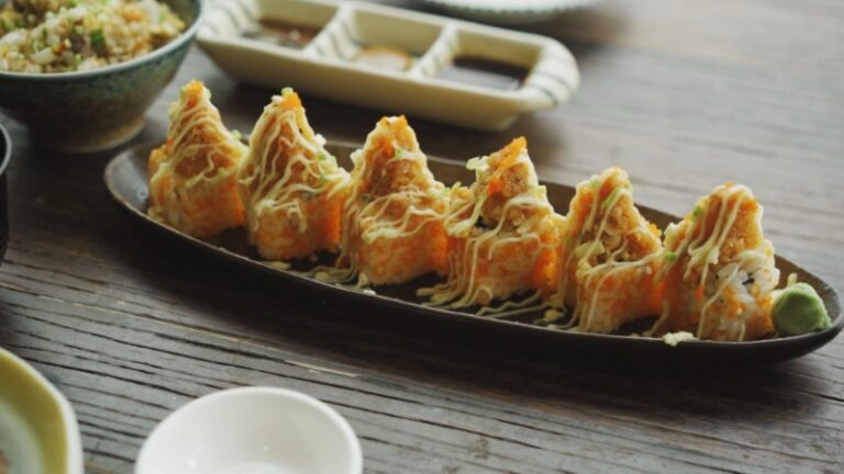 Crispy sushi rolls topped with creamy drizzle on a dark platter highlight elegant restaurant presentation
