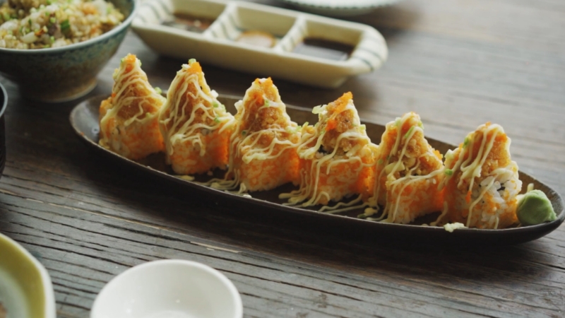 Crispy sushi rolls topped with creamy drizzle on a dark platter highlight elegant restaurant presentation