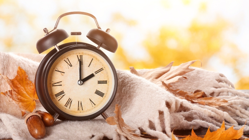 Alarm clock on a blanket with autumn leaves, showing daylight saving time change