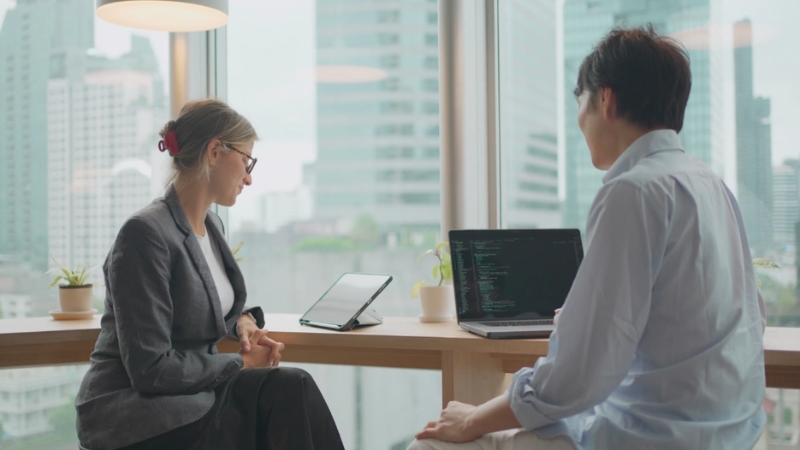 A manager and developer discuss hiring and training plans for a software engineering team in a modern office setting