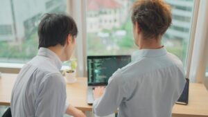 Two developers review code together on a laptop as part of a software engineering team