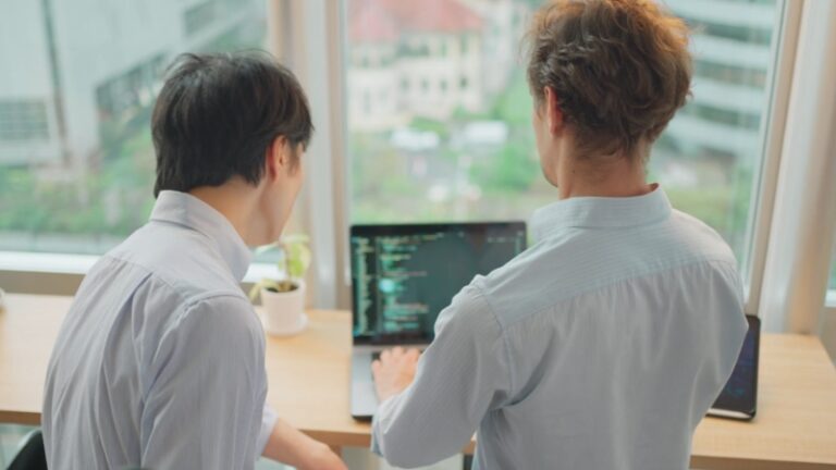 Two developers review code together on a laptop as part of a software engineering team