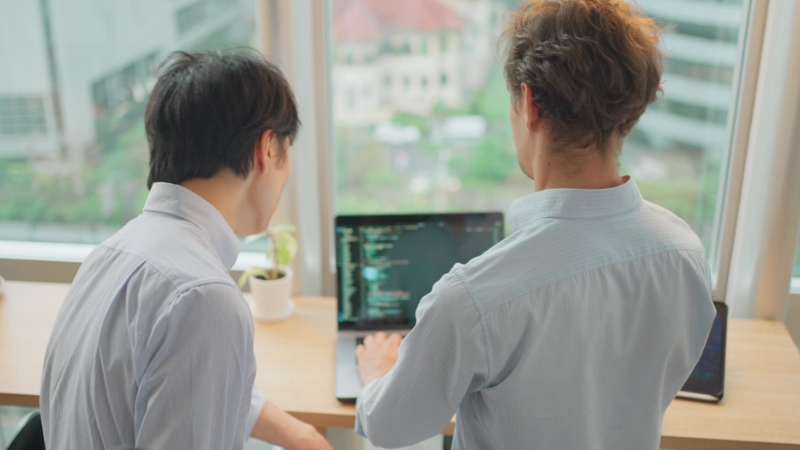 Two developers review code together on a laptop as part of a software engineering team