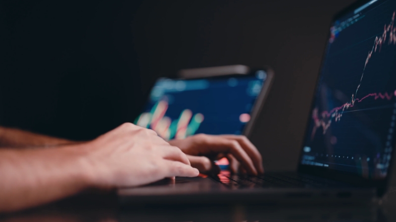 Hands typing on a laptop with financial charts on the screen, illustrating KYC standards for crypto and fintech oversight