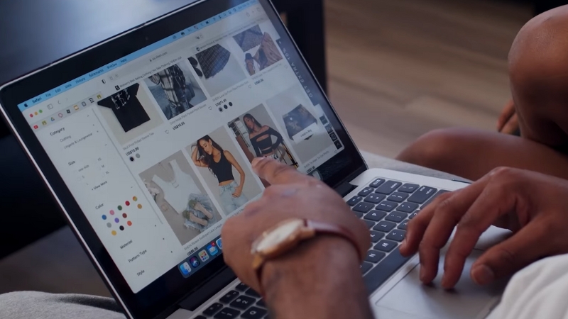 A person scrolls through clothing listings on a laptop, choosing products for an online shop
