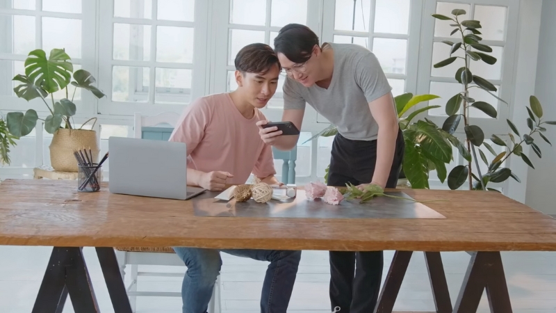 Two people review product details on a phone at a table with craft materials while planning an online shop