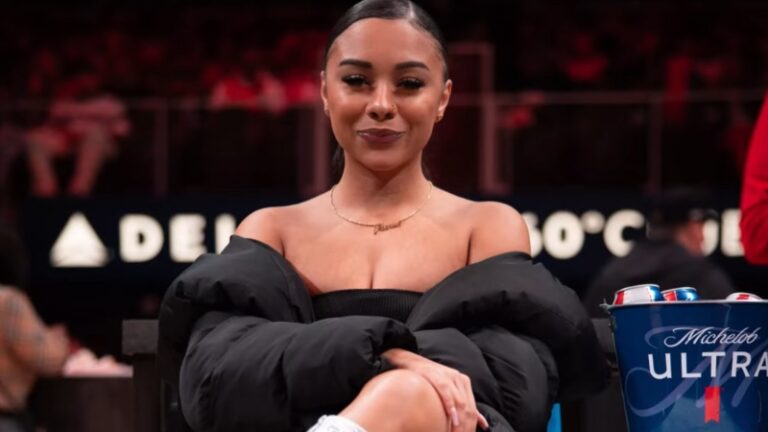 Alix Lapri sitting courtside at an event, smiling with her arms crossed