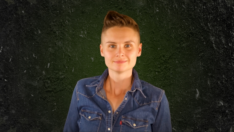 Ashley Gutermuth wearing a denim shirt and standing against a dark green textured background