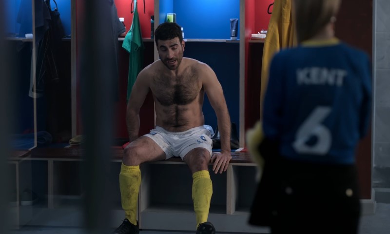 Shirtless Brett Goldstein sitting in a locker as Roy Kent