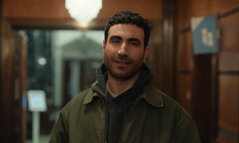 Brett Goldstein in a green jacket stands in a hallway
